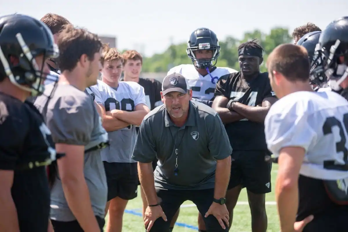A football coach motivating players during a team huddle on a college football practice field