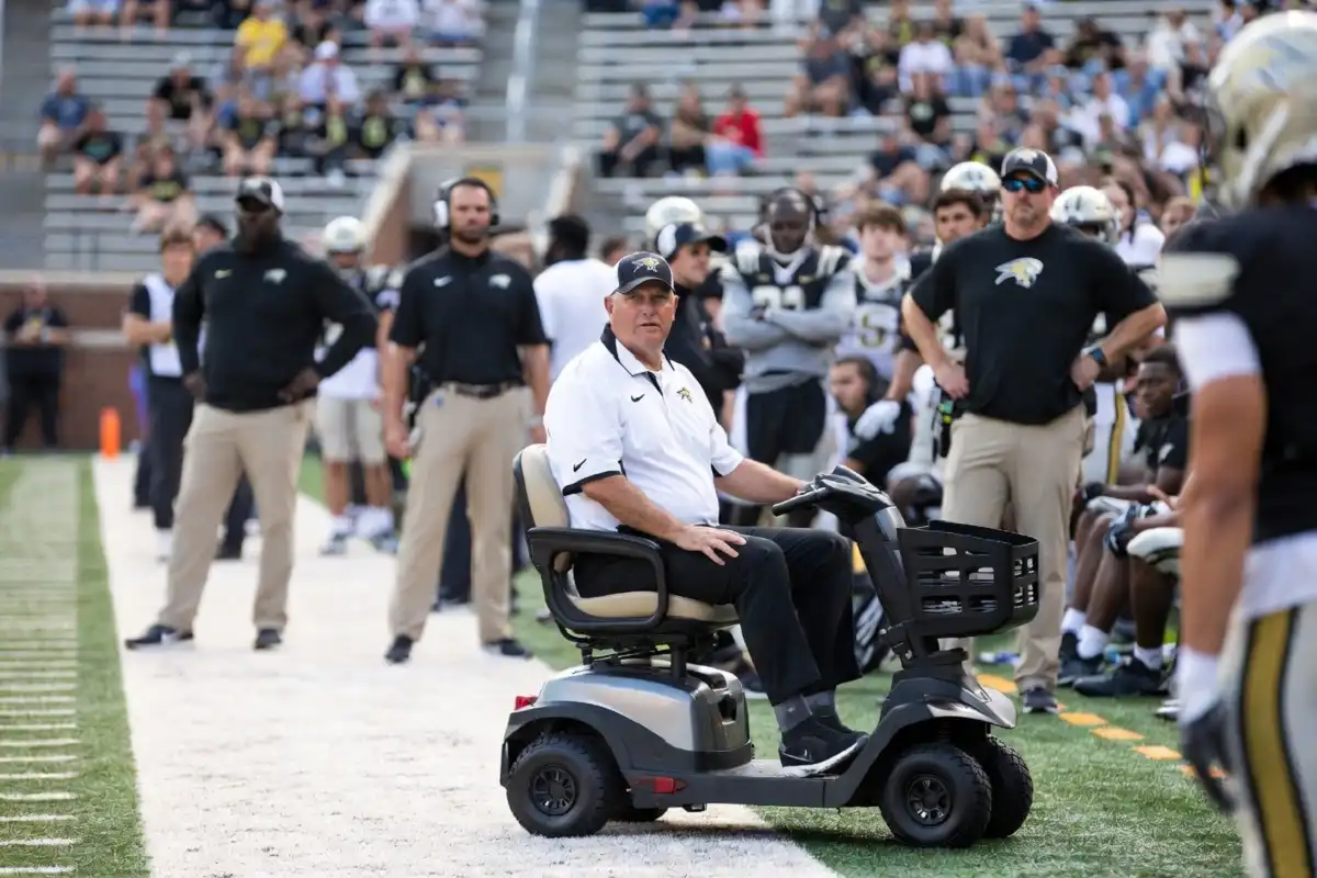 A football coach using a mobility scooter on a college football sideline during a game